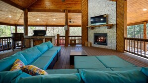 A wooden deck with a sofa, a fireplace, and a TV mounted on a brick wall. - Sleeps 24 * Luxe Pool Cabin Secluded w/Game Room (Broken Bow)