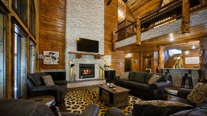 A spacious living room with leather sofas, a stone fireplace, and a wooden ceiling. - Sleeps 24 * Luxe Pool Cabin Secluded w/Game Room (Broken Bow)
