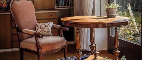 A cozy reading nook with a wooden chair, a round table, and a bookshelf filled with books.