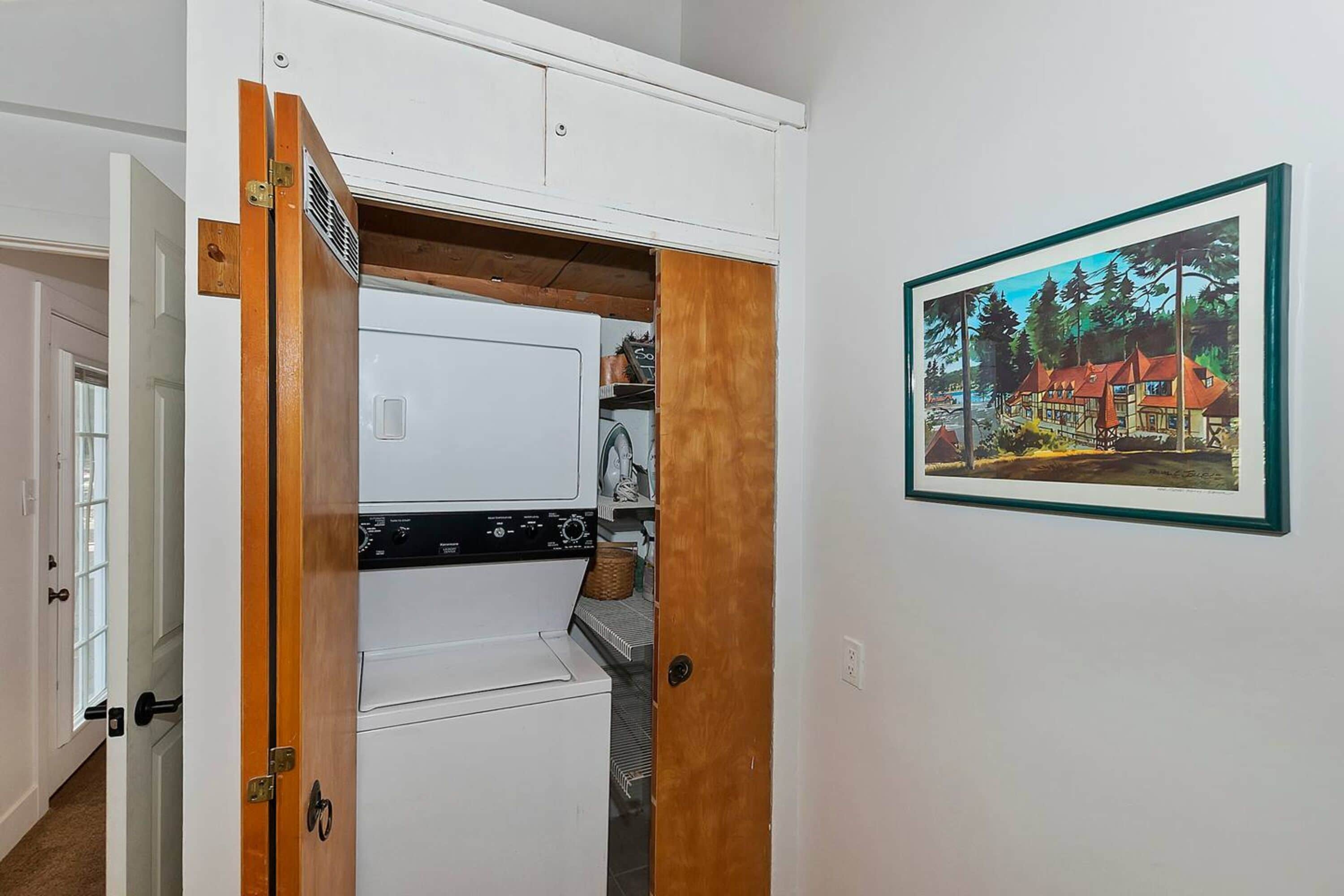 A compact laundry room with a washer and dryer, a wooden door, and a framed painting on the wall.