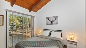 A bedroom with a large bed, a view through a sliding glass door, a wooden ceiling, and a deer head artwork on the wall. - Peaceful Sunshine Chalet with Hot Tub (Big Bear Lake)