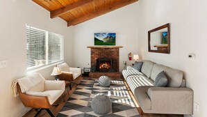 A cozy living room with a fireplace, a sofa, a chair, and a patterned rug. - Peaceful Sunshine Chalet with Hot Tub (Big Bear Lake)