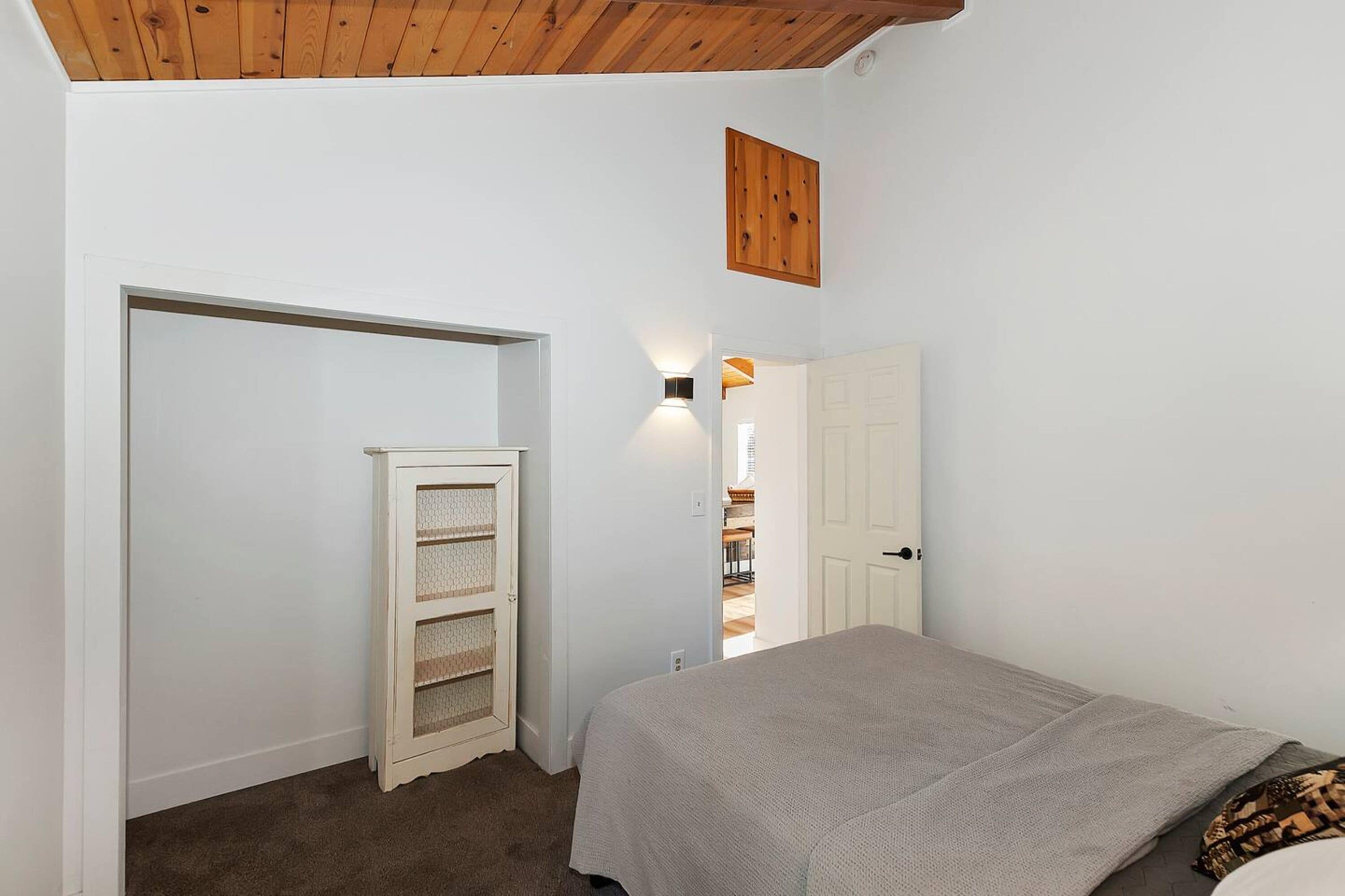 A bedroom with a bed, a wardrobe, a shelf unit, and a door leading to another room.