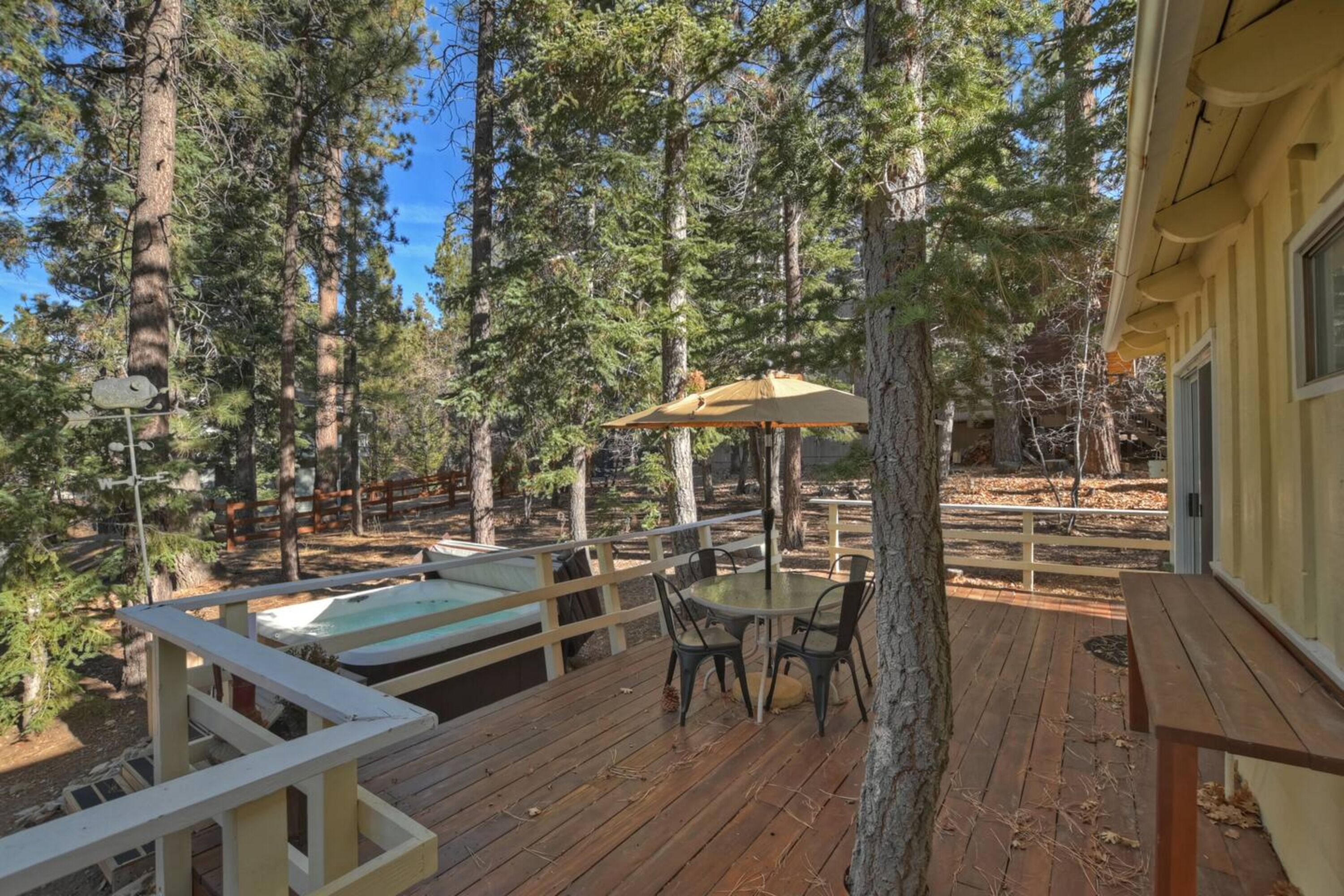 A wooden deck with a table and chairs, surrounded by tall pine trees.