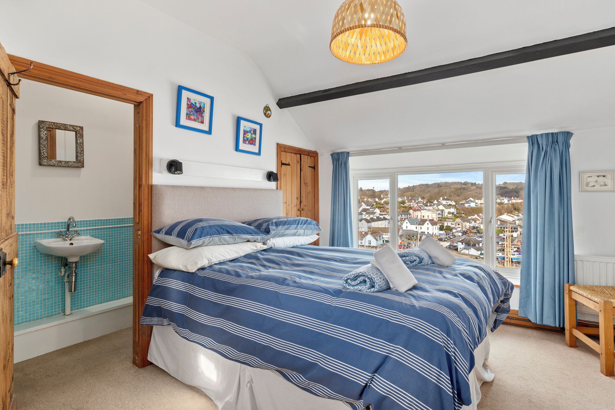 Ein Schlafzimmer mit einem großen Bett, einer Holzbank, Blick auf die Stadt durch das Fenster und einer Hängeleuchte.