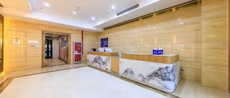 A hotel reception area with marble counters, a wooden reception desk, and a tiled floor.