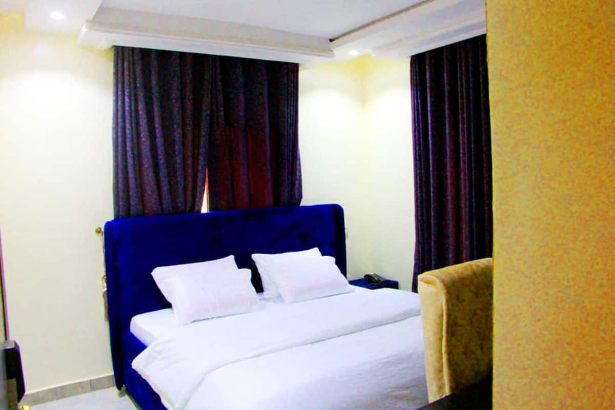 Habitación de hotel con una cama grande, cortinas oscuras y un cabecero azul.
