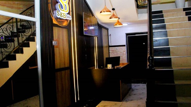 A hotel reception area with a staircase, a reception desk, and a sign for S&B Suites. - S and B Suites (Lagos)