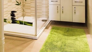 Une salle de bain avec une douche à parois de verre, un lavabo blanc et un tapis vert.