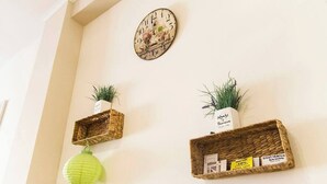 Un mur orné d’une horloge décorative, deux étagères en osier avec des plantes et une lanterne verte suspendue.