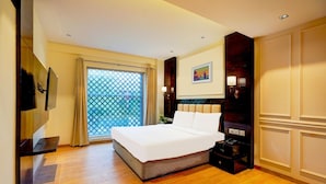 A hotel room with a large bed, a TV mounted on the wall, a desk with a lamp, and a window with curtains. - Palette South Delhi Imperial Villa (New Delhi)