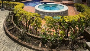 A circular pool with a fountain, surrounded by a brick pathway and lush greenery. - Finca hotel el diamante (Calarcá)