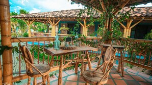 An outdoor patio with wooden tables and chairs, surrounded by bamboo structures and greenery. - Finca hotel el diamante (Calarcá)