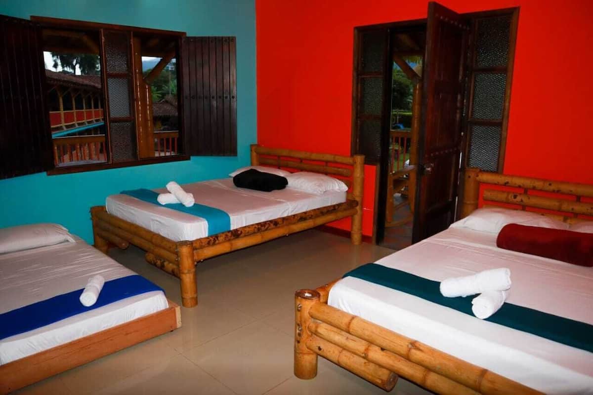 A room with three wooden beds, each with white bedding and a rolled towel.