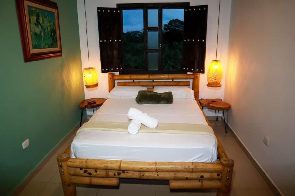 A neatly made bed with white linens and two rolled towels, a wooden headboard, and two bedside tables with lamps.