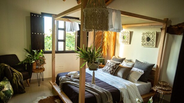 A four-poster bed with a wooden frame, a hanging macrame light fixture, and a view of the outdoors through a window with curtains. - Finca hotel el diamante (Calarcá)