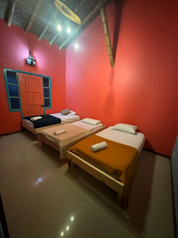 A room with four single beds, a red wall, a wooden door with blue trim, and a ceiling with exposed beams and hanging lights. - Finca hotel el diamante (Calarcá)