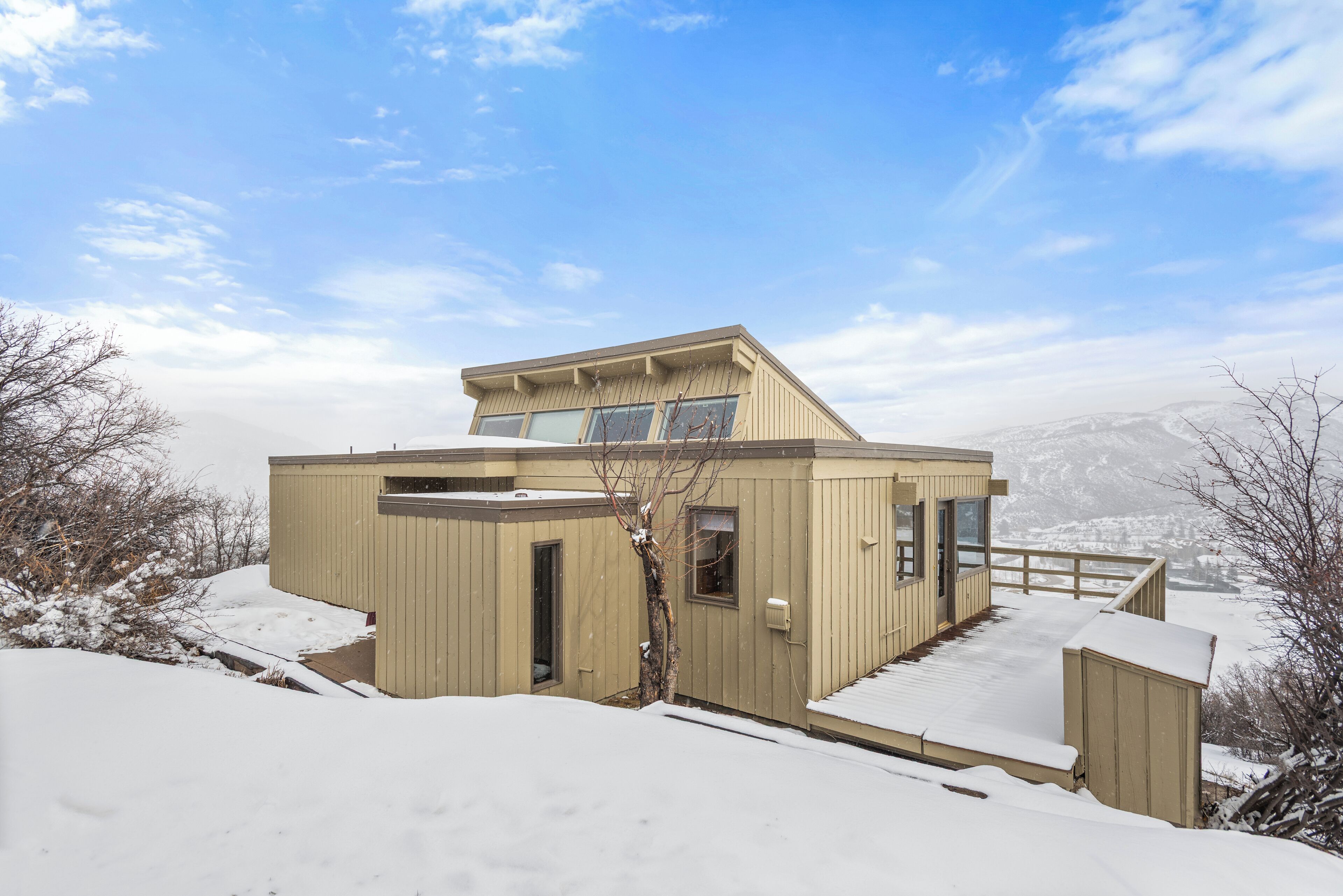 Eine Holzhütte mit geneigtem Dach und großen Fenstern, umgeben von verschneiter Landschaft und Bergen.