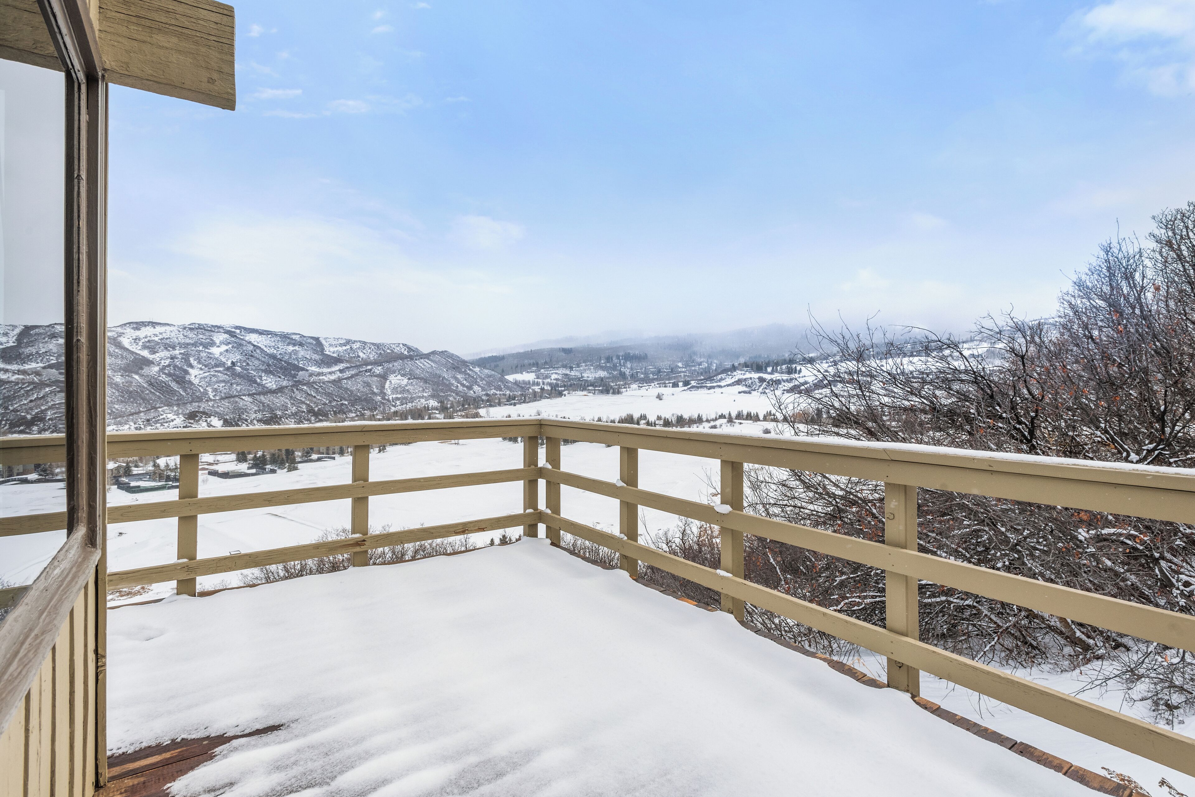 Un balcon doté d’une balustrade en bois, d’où l’on peut admirer un paysage enneigé avec des montagnes et un ciel dégagé.