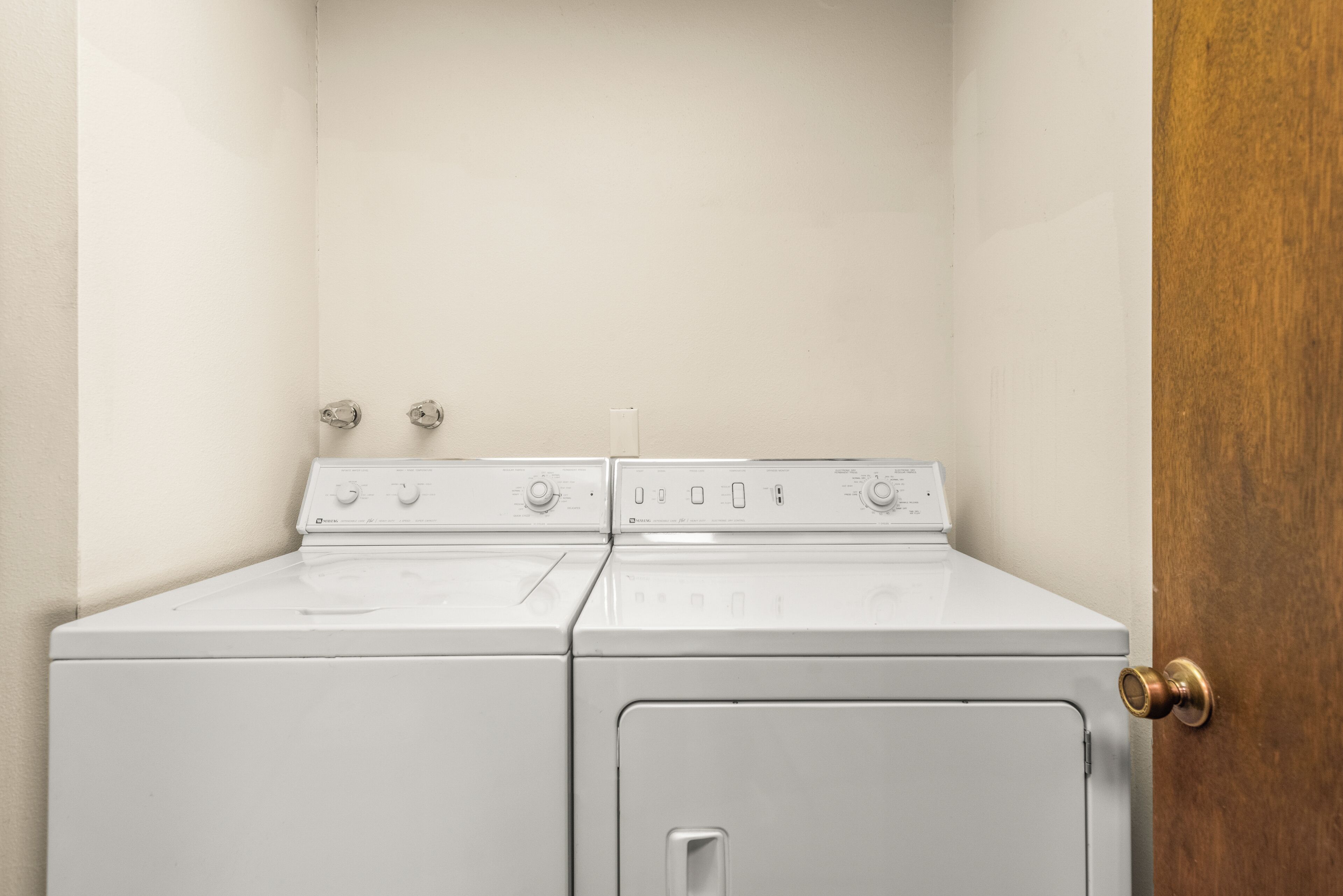 A laundry room with two stacked washers and dryers, a wooden door, and a white wall.