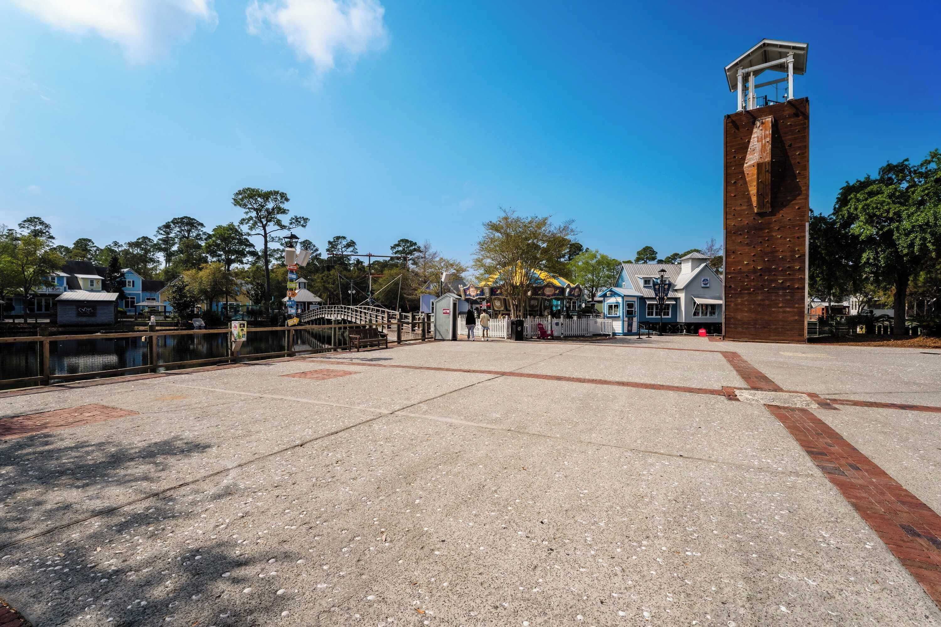 A spacious plaza with a tall brick tower, a bridge, and a Ferris wheel in the background.
