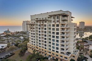 A multi-story hotel with balconies, a parking area, and a view of the sea.