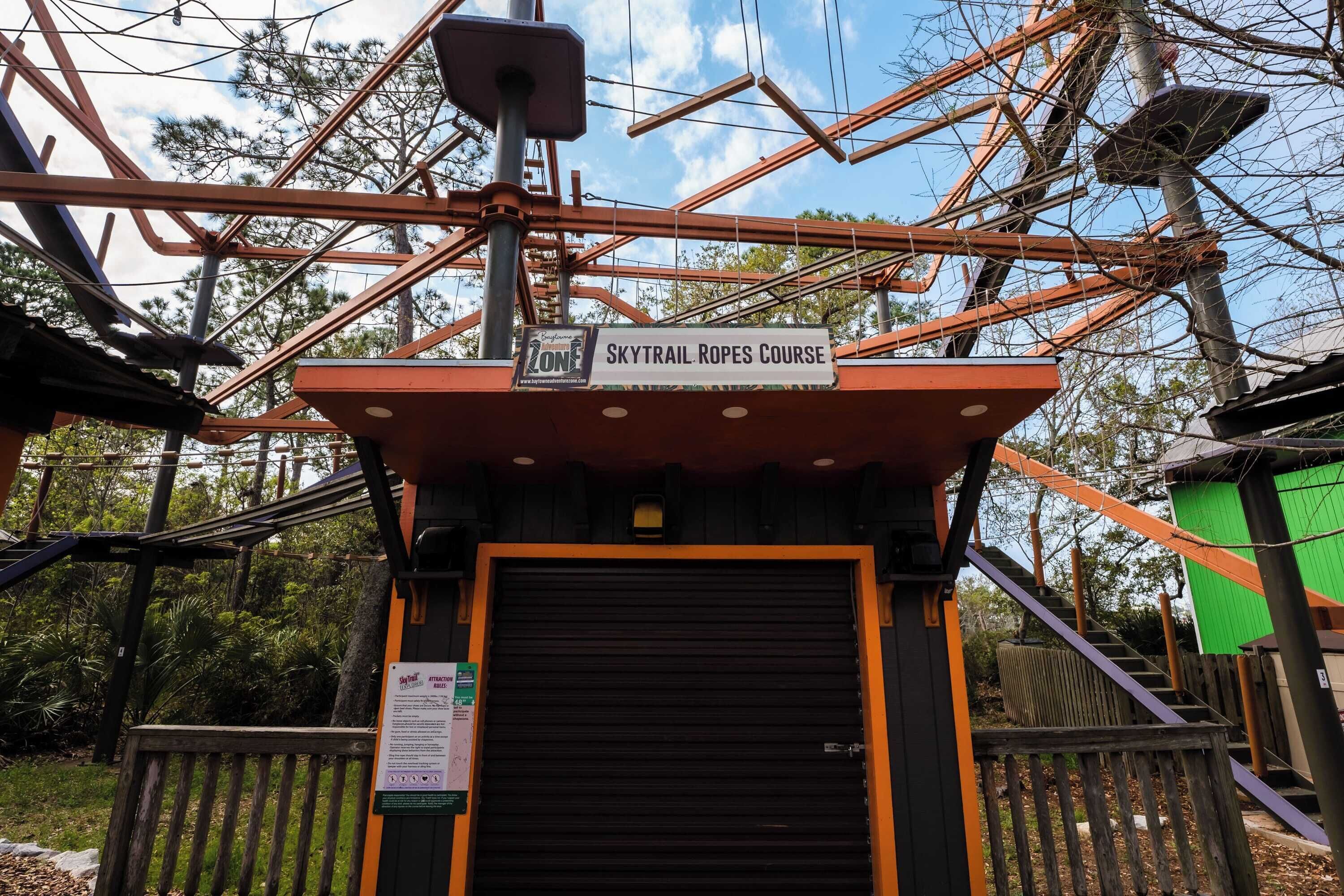 Entrada de una montaña rusa con un cartel que anuncia el Campo de Cuerdas Skytrail.