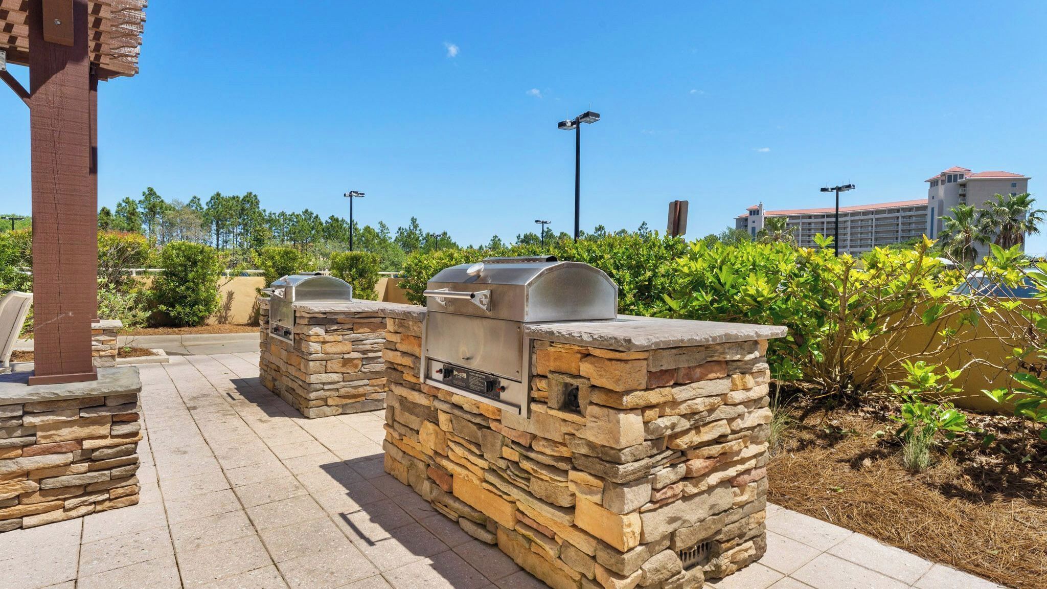 Outdoor barbecue grills with stone walls, a paved walkway, and a clear sky.