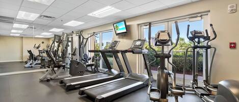 Un gimnasio con cintas de correr, elípticas y una pantalla de televisión.