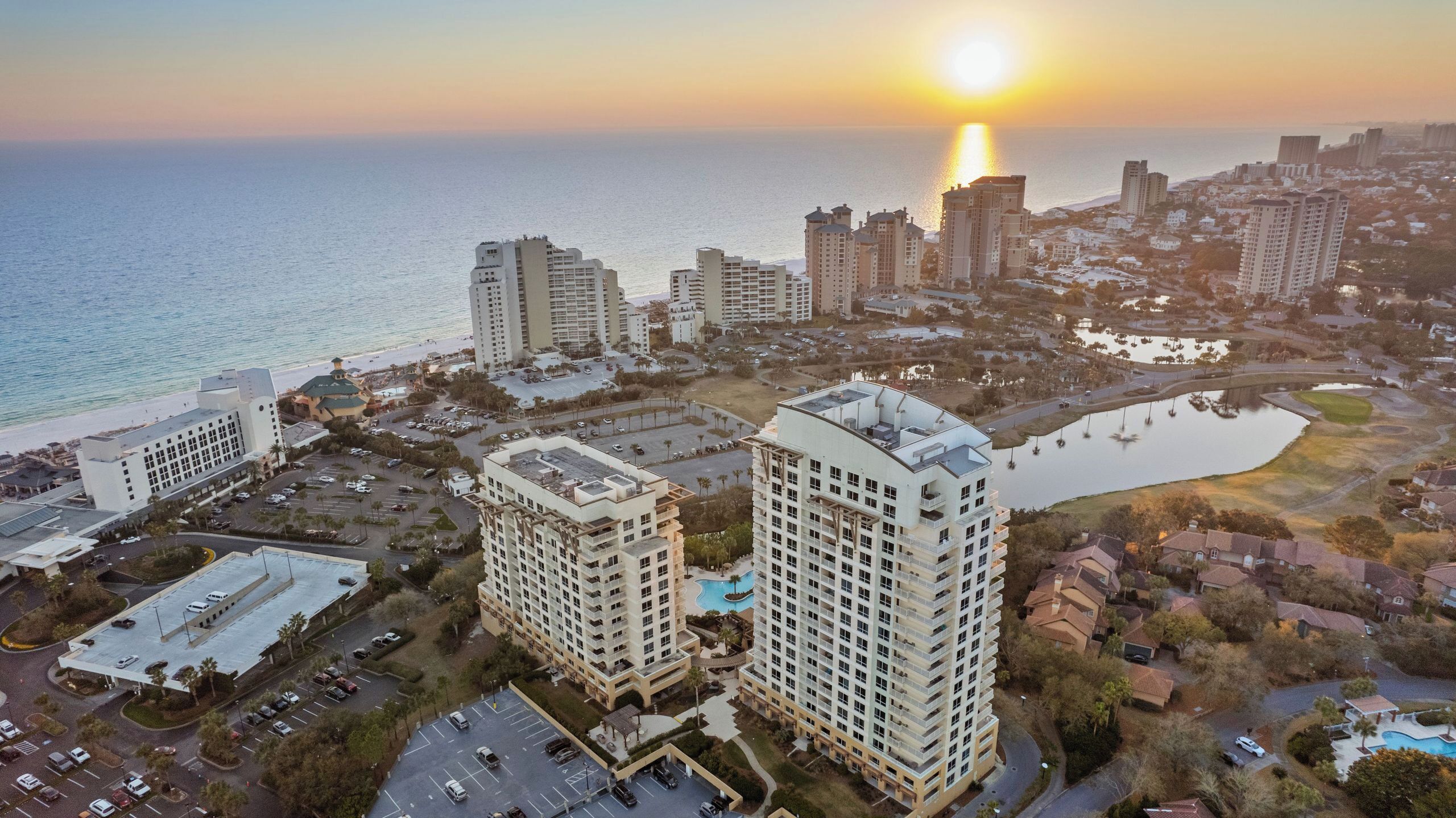 A high-rise hotel with a swimming pool, located near a beach and a body of water.