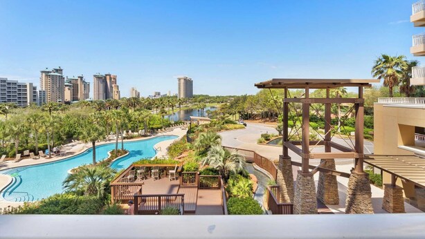 A resort with a large swimming pool, palm trees, and a view of tall buildings in the background. - Miramar Beach Studio w/ Pool, Tennis & Walk to Beach Luau Eastern Sky (Miramar Beach)