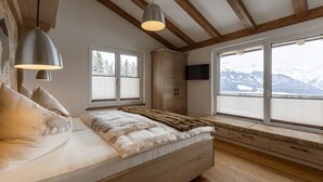 A bedroom with a bed, wooden beams, a window with a view of mountains, and a mounted TV. - Penthouse Near Mittersill (Mittersill)