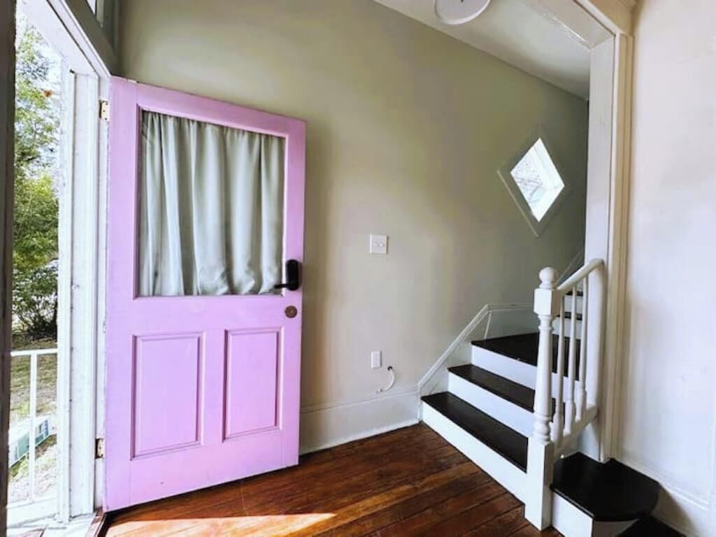 Une pièce avec une porte rose, un escalier et une fenêtre.