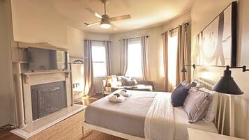 Une chambre à coucher avec un lit, un ventilateur de plafond, une cheminée, un téléviseur et une fenêtre.