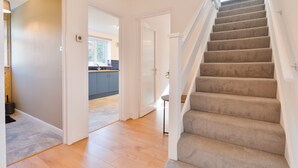 A staircase leading to an upper floor, a kitchen area with blue cabinets, and a door leading to another room. - Stylish 4 Bedroom Spacious House w/ Parking - Sleeps 10 - Families & Contractors (Broad Oak)