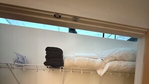 Una piccola stanza privata con un letto a castello, uno scaffale bianco con asciugamani piegati e una finestra sopra il letto.