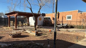 A backyard with a pergola, patio furniture, a tree, and a brick wall. - Cozy North Valley Charm (Albuquerque)