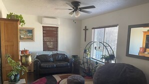 A living room with a black leather sofa, a wooden cabinet, a ceiling fan, and a window with blinds. - Cozy North Valley Charm (Albuquerque)