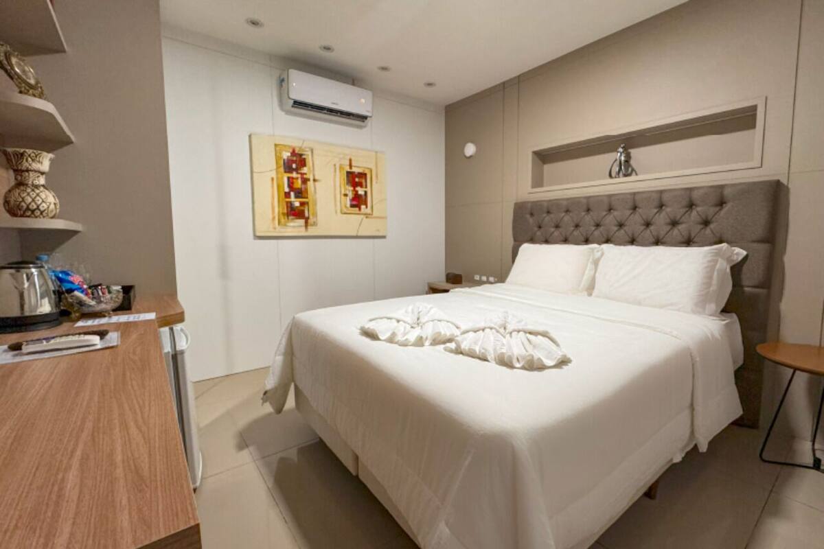 Una camera d'albergo con un letto grande, una scrivania in legno, un condizionatore d'aria a parete e due opere d'arte incorniciate.