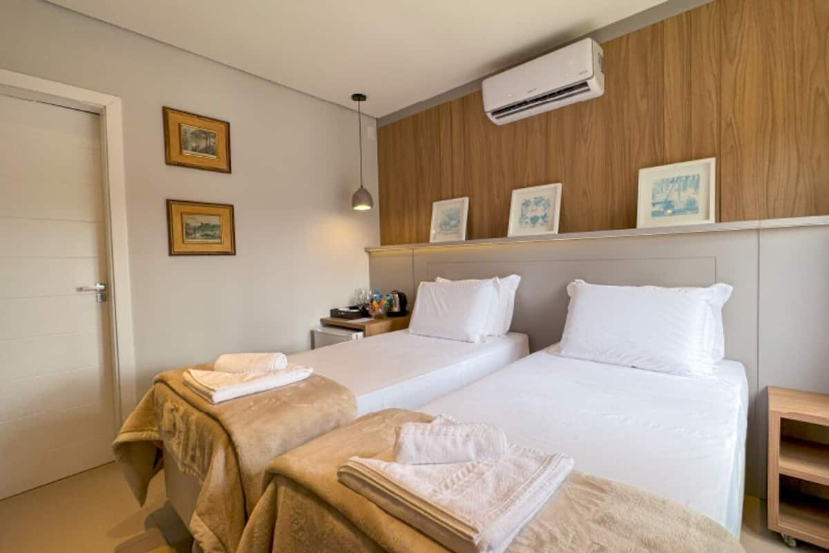 Camera d'albergo con due letti, una testiera in legno, un condizionatore d'aria a parete e quadri appesi.