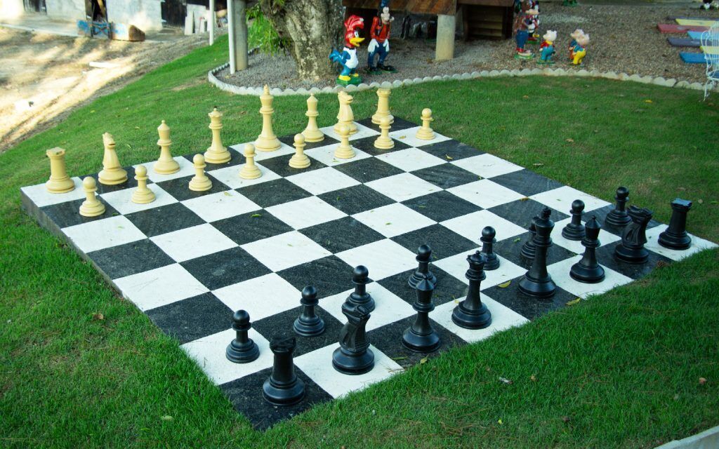 A large outdoor chessboard set up on a grassy lawn.