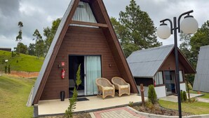 Un edificio moderno de forma triangular con fachada de madera, puerta de vidrio y dos sillas de mimbre en el exterior.