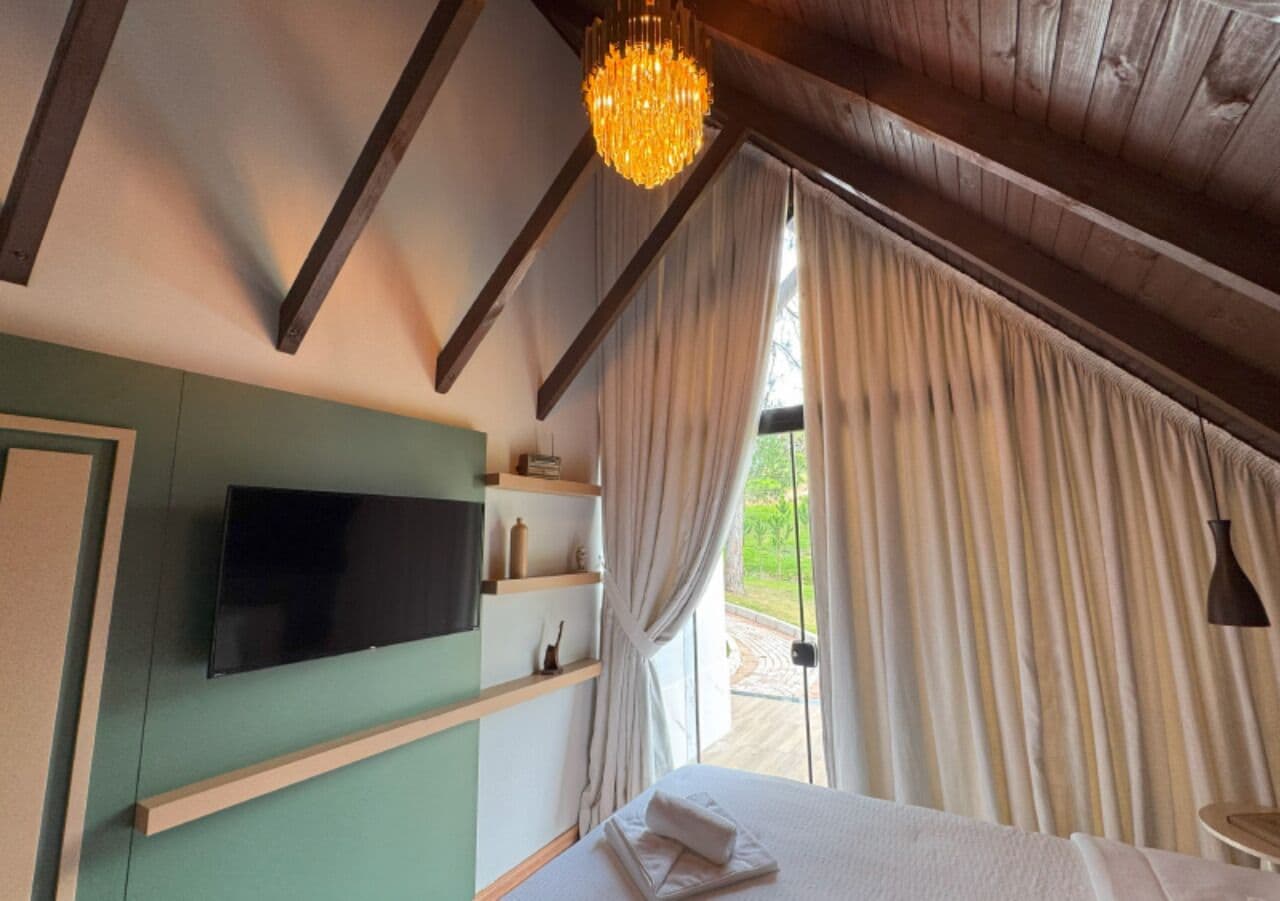 Een slaapkamer met een bed, een wandtelevisie en een raam met gordijnen.