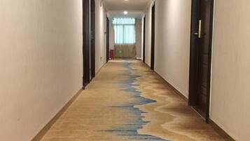 A hotel hallway with a carpeted floor, doors on both sides, and a window at the end.