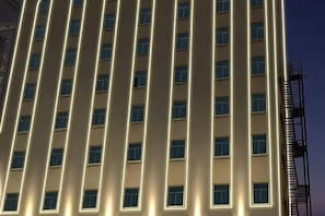 A tall building with evenly spaced windows and a vertical light strip running down the center. - Anxin Chengji Hotel (Jinjiang Shoes Store) (Jinjiang)