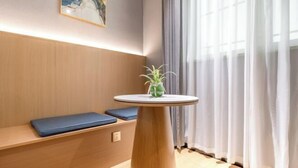Una habitación con un banco de madera, una pequeña mesa redonda con una planta y un cuadro en la pared.