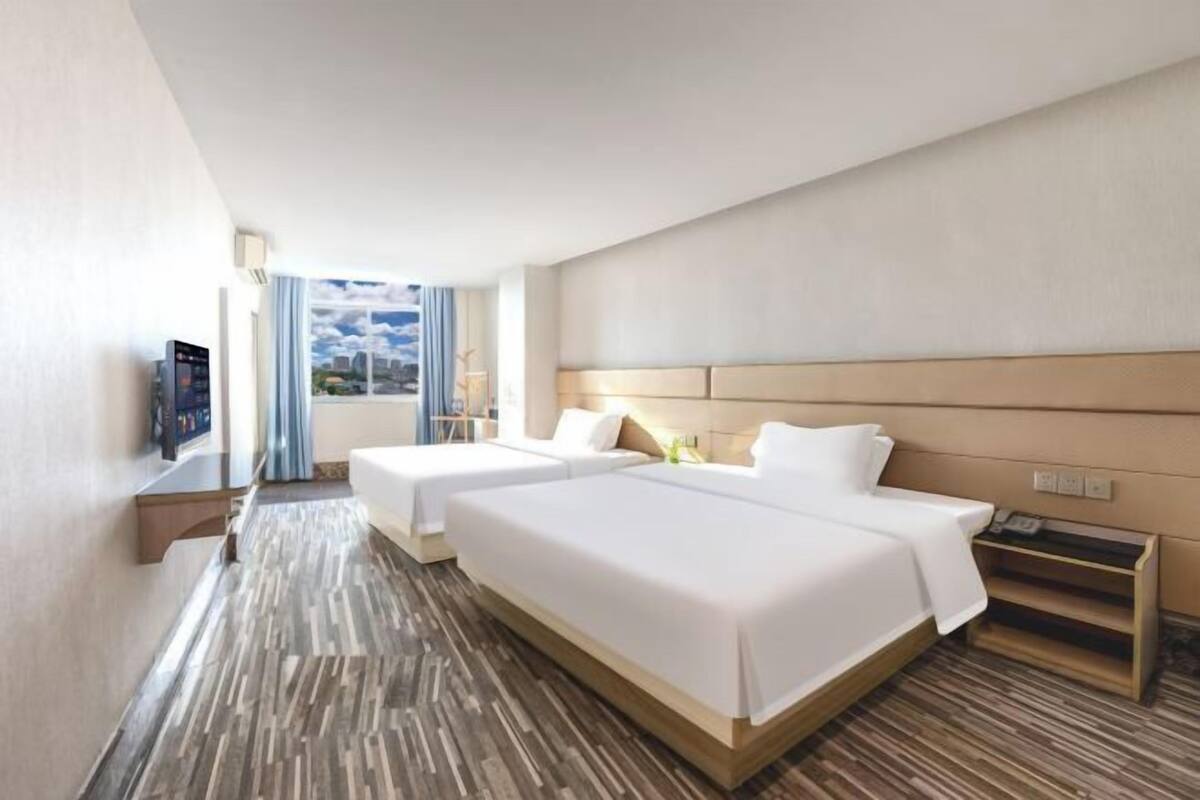 A hotel room with two beds, a TV, a window with curtains, and a wooden floor.