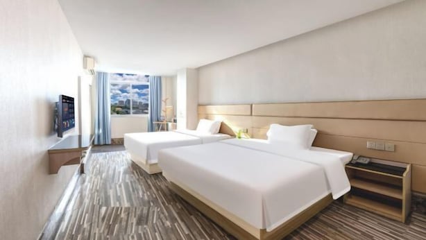 Habitación de hotel con dos camas, televisión, ventana con cortinas y suelo de madera.