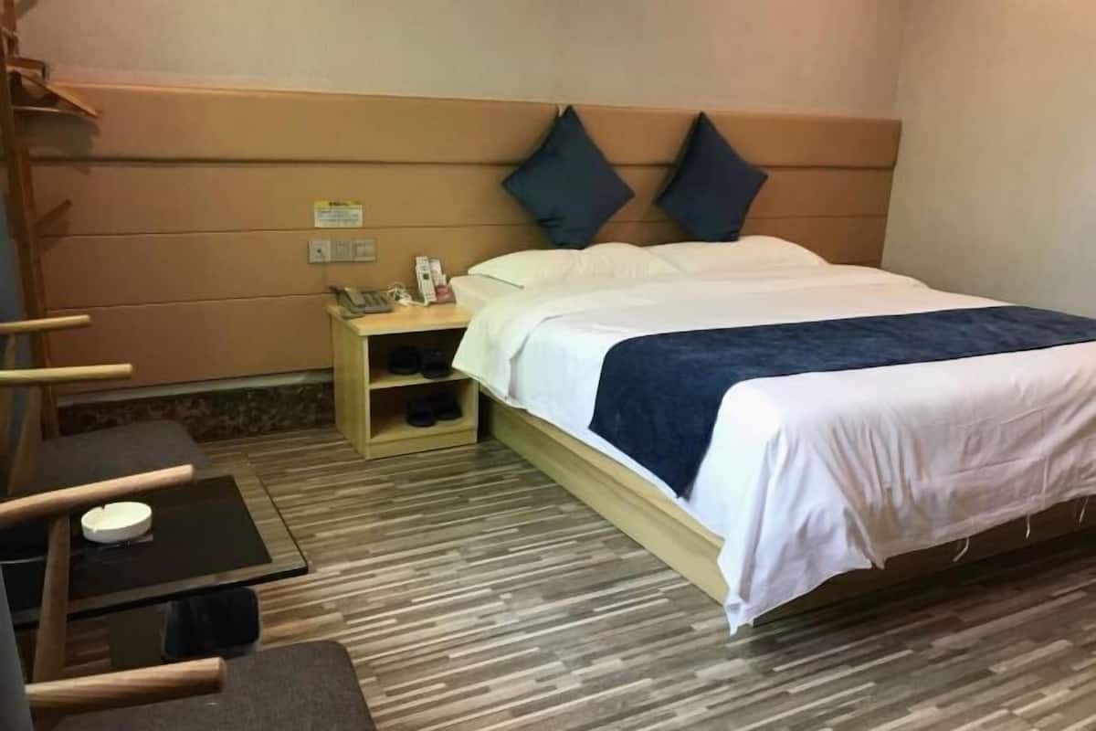 A hotel room with a bed, a nightstand, a chair, a small table, and a shoe rack.