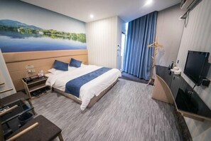 Een hotelkamer met een bed, een bureau, een televisie en een schilderij van een meer.